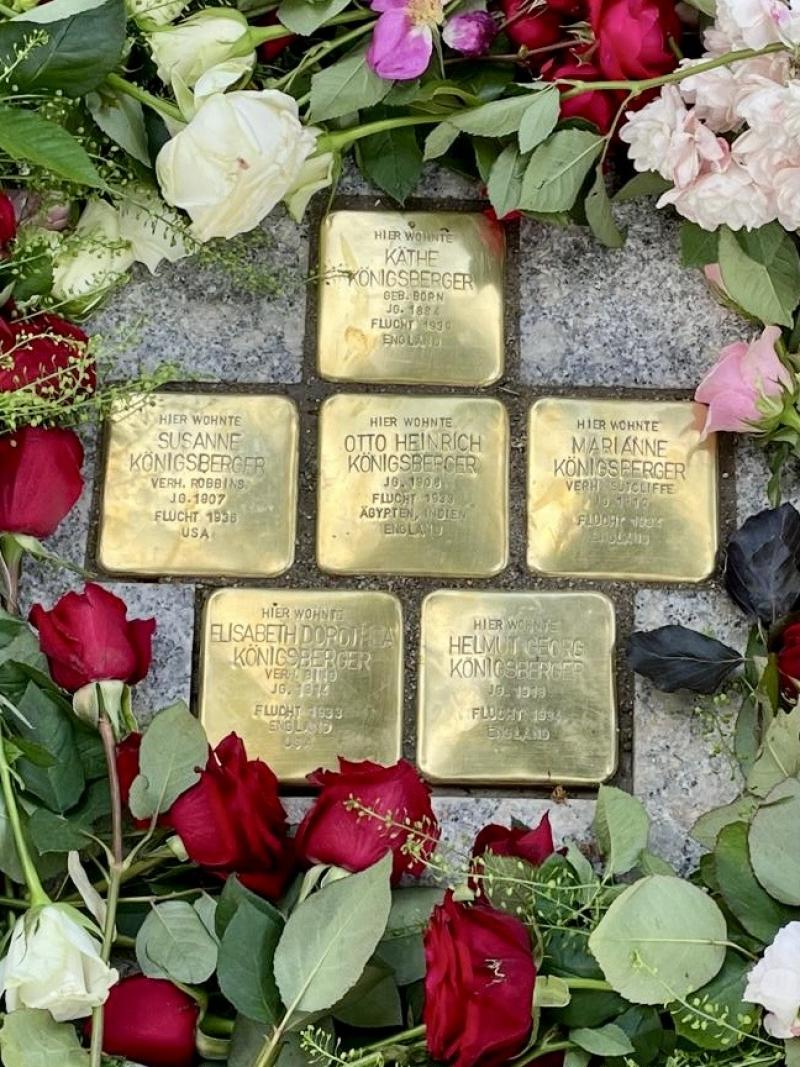 Sechs Stolpersteine liegen im Boden, umrankt von Blumen.