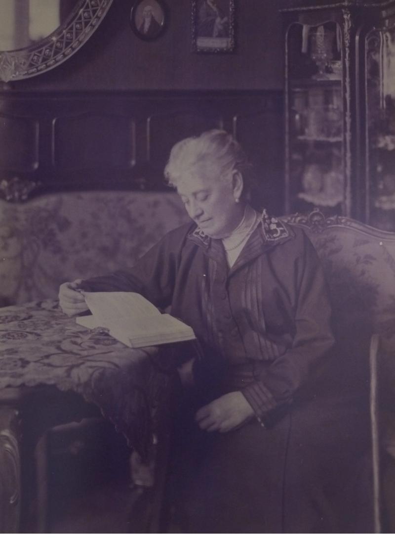 Elise Gutkind sitzt an einem Tisch in einem gutbürgerlichen Wohnzimmer und liest in einem Buch