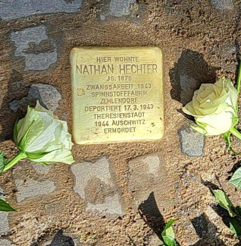 Bild des Stolpersteins, umrahmt mit weißen Rosen.
